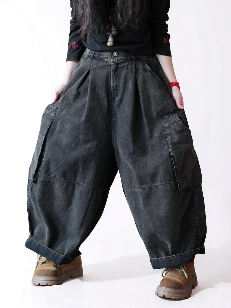 May include: Charcoal gray denim pants featuring a high-waisted design with front pleats, a button closure, and two large side cargo pockets. These wide-leg trousers have a relaxed, voluminous silhouette with cuffed hems and a faded wash finish.