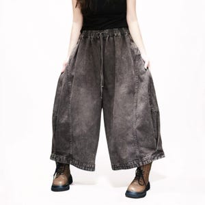 May include: Wide-leg trousers in a dark charcoal grey acid-wash denim fabric. These loose-fitting trousers feature an elasticated waistband with a drawstring closure, vertical seam detailing down the front, and a cropped length that hits above the ankles.