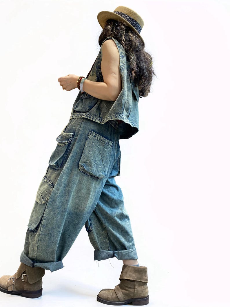 May include: A denim vest and matching cargo pants in a light blue wash. The pants have large pockets and are cuffed at the ankles. A straw hat with a patterned band and brown suede boots complete the outfit. The outfit is casual and stylish.