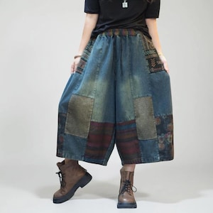 May include: Wide-leg denim trousers featuring a patchwork design with various fabric textures, including blue denim, brown plaid, and floral patterns. The trousers have an elastic waistband with a drawstring and a loose, relaxed fit that falls below the knee.