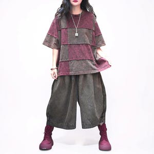 May include: A short-sleeved t-shirt featuring a patchwork design of maroon and dark grey panels, paired with loose-fitting, wide-leg cropped trousers in a matching dark grey tone. The outfit is completed with a pair of maroon lace-up boots.