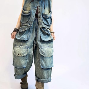 May include: A denim vest and matching pants set in a light blue wash. The vest has multiple pockets and a hood. The pants are loose-fitting with large pockets and rolled-up cuffs. The outfit is worn with brown boots.