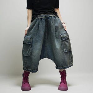 Könnte beinhalten: Weit geschnittene blaue Cargo-Hose aus Denim mit verwaschener Optik, elastischem Bund mit Kordelzug, zwei großen seitlichen Cargotaschen mit Klappen und einem tief sitzenden Schritt, die in einer verkürzten Länge über den Knöcheln endet.