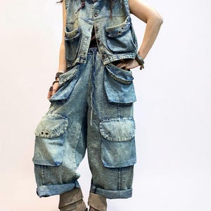 May include: A denim vest and matching cargo pants set in a light blue wash. The vest has multiple pockets and button closures. The pants feature large pockets and a drawstring waist. The outfit is paired with brown boots.