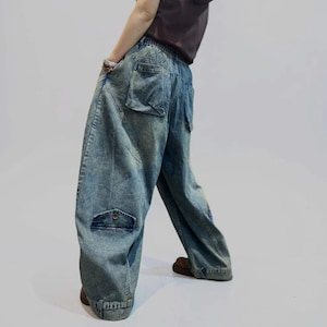 Könnte beinhalten: Weit geschnittene blaue Jeans aus Denim mit Acid-Wash-Effekt, elastischem Bund und mehreren Utility-Taschen. Die Hose verfügt über eine auffällige Pattentasche an der Beinaußenseite sowie eine Gesäßtasche und zeichnet sich durch einen lockeren Schnitt aus.