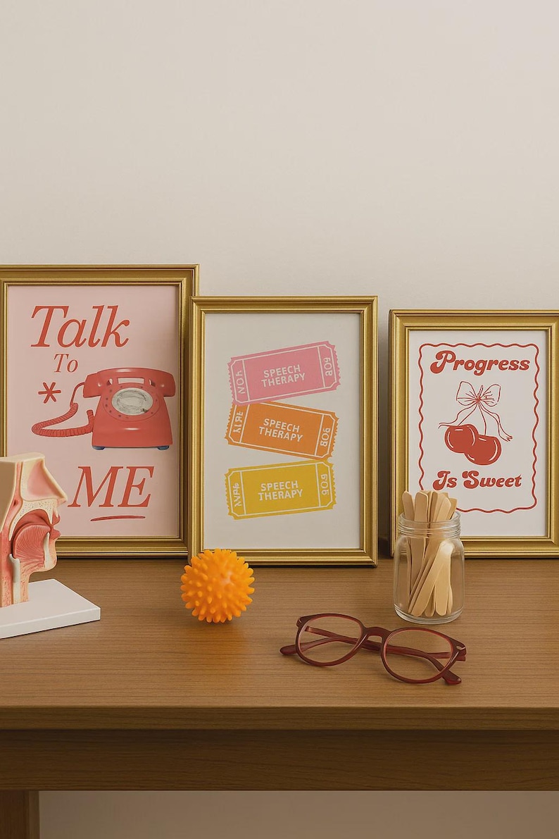 May include: Three framed prints with gold frames on a wooden surface. One print says "Talk To Me" with a red telephone graphic. Another has "Speech Therapy" tickets. The third says "Progress Is Sweet" with cherries.