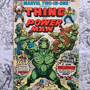 Può includere: Fumetto Marvel Two-In-One con "The Thing" e "Power Man." La copertina presenta una grande figura verde con la scritta "I AM BRAGGADOOM!" e altri personaggi. Il fumetto è datato gennaio 1975.