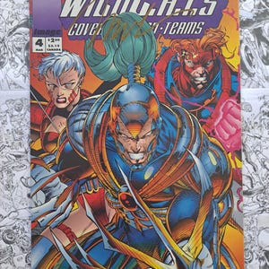 May include: WildC.A.T.S. comic book cover featuring three costumed characters in a dynamic action pose. The cover art is vibrant with a purple, orange, and blue color scheme. The comic book is signed.