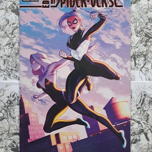 May include: Comic book cover for Edge of Spider-Verse #3, Variant Edition. Features two Spider-Woman characters in dynamic poses against a cityscape and sky background. The cover art is vibrant with a mix of blues, purples, and pinks.