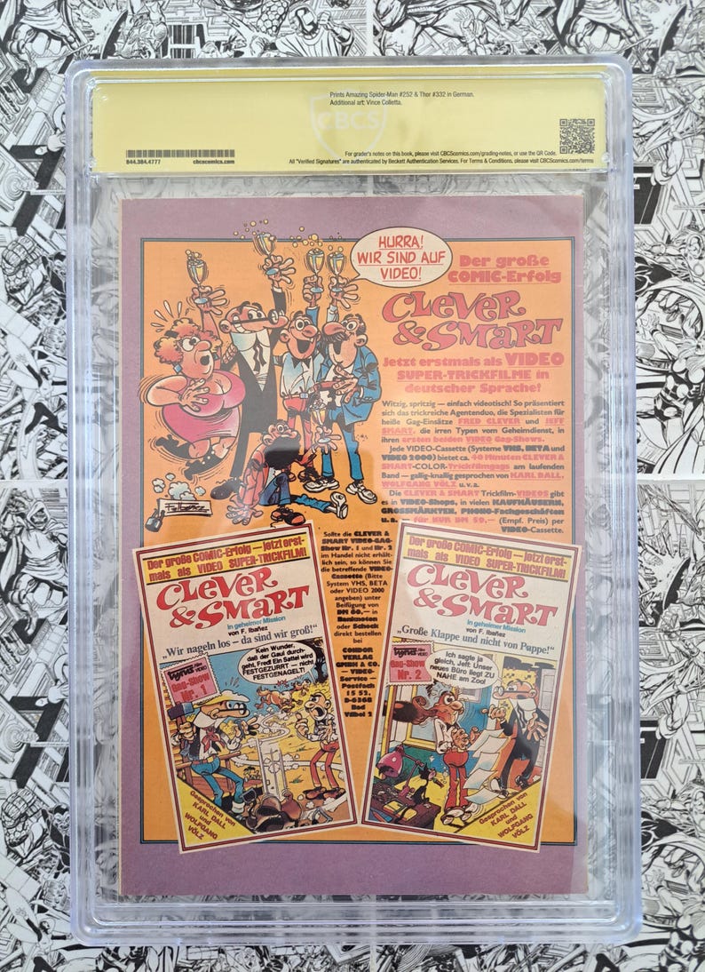 May include: A comic book cover featuring the characters from "Clever & Smart" in a German advertisement. The cover is encased in a protective holder. The advertisement includes text in German, promoting the video release of the comic.