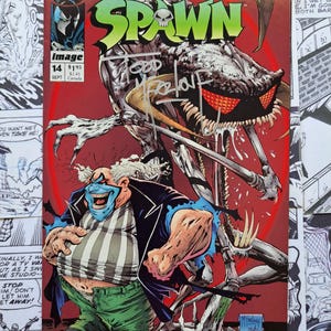 May include: Spawn comic book cover featuring a grotesque creature with red eyes and a skeletal figure. The cover includes the title "SPAWN" in green, issue number 14, and the Image Comics logo. Signed by Todd McFarlane.