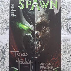 May include: Spawn comic book cover featuring a split image of the character's face with glowing green eyes and a skull. The title "Spawn" is in green, and the cover includes signatures and the text "Pre-Sale Printer Sample."