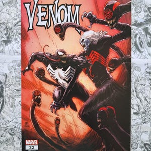 May include: Comic book cover featuring the word "Venom" in white, with a red and orange background. The artwork depicts two Venom characters in a battle scene, with tentacles and sharp teeth. The Marvel logo and issue number 32 are visible.