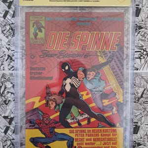 May include: A comic book titled "Die Spinne #111" in a protective case. The cover features Spider-Man in a black costume, with German text and the Marvel Comics logo. The comic is graded 7.5 by CBCS.