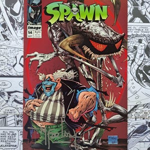 May include: Comic book cover for Spawn #14, featuring a monstrous creature with red eyes and a clown character. The title "SPAWN" is in green and red. The cover has a red background and includes the Image Comics logo.