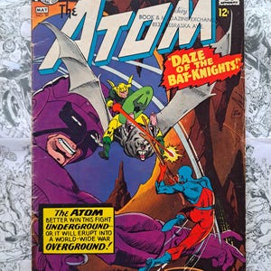 May include: Vintage comic book cover of "The Atom" featuring a battle scene with the text "Daze of the Bat-Knights!" and "The Atom Better Win This Fight Underground". The cover has a purple, blue, red, yellow, and green color scheme.