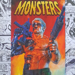 May include: Comic book cover titled "MONSTERS" by Mark Spears. The cover features a muscular figure holding two large guns. The figure has cybernetic enhancements and is set against a fiery orange background. The comic is labeled "#8 Blind Bag Variant".