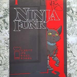 May include: Comic book cover for "Ninja Funk" featuring a robotic cat with yellow eyes and a blue collar. The title is in white letters with a black background, and the number "1" is in red. The cover is signed.