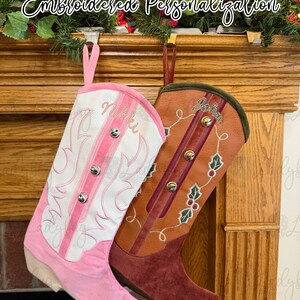 May include: Two personalized cowboy boot Christmas stockings. One is pink and white with the name "Niki" embroidered. The other is brown with the name "John" embroidered, and holly berry accents. The text "Embroidered Personalization" is above.
