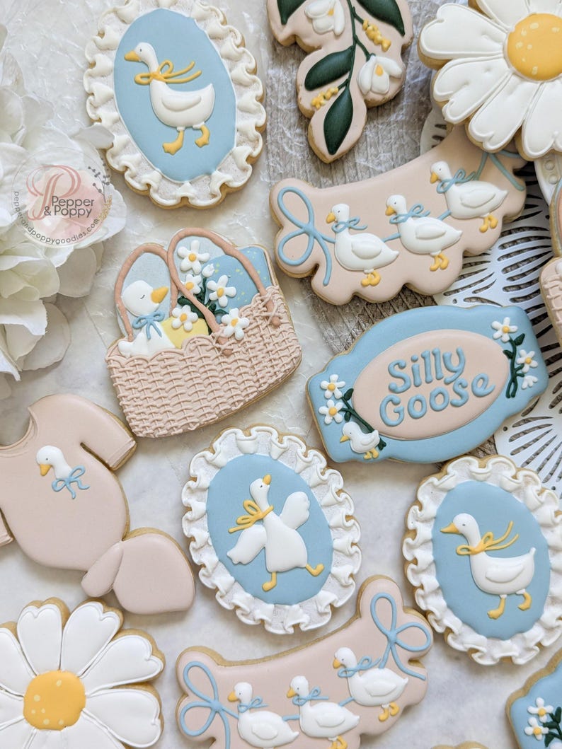 May include: Assortment of decorated sugar cookies with a baby shower theme. Cookies include a onesie, daisies, and oval cookies with a goose design. Colors include white, light blue, yellow, and tan.