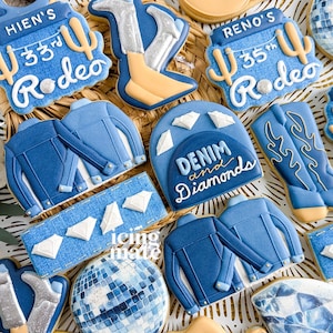 May include: An assortment of decorated sugar cookies with a denim and diamonds theme. The cookies feature cowboy boots, jackets, disco balls, and cowboy hats. Some cookies have text that reads "Denim and Diamonds" and "Reno's 35th Rodeo."
