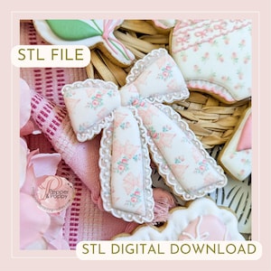 May include: Close-up of decorated cookies in the shape of a bow, a onesie, and other shapes. The bow cookie has a white base with a pink bow and floral pattern. The text "STL FILE" and "STL DIGITAL DOWNLOAD" are visible.