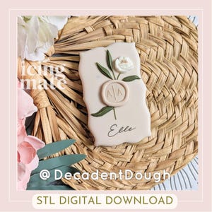 May include: A light beige cookie decorated with a white flower, green leaves, and a circular emblem with the letters "AA". The word "Elle" is written in cursive. The cookie is on a woven background. The text "STL DIGITAL DOWNLOAD" is at the bottom.
