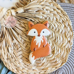 Pu&ograve; includere: Un biscotto a forma di volpe decorato con glassa arancione, bianca e marrone. Il biscotto &egrave; posto su un sottobicchiere intrecciato di colore naturale. Il biscotto ha un design dettagliato, con pancia e punta della coda bianche. Una dolcezza.