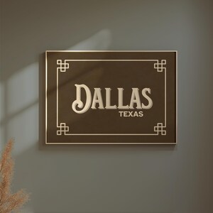 Pu&ograve; includere: Un cartello rettangolare marrone con la scritta "DALLAS" in un carattere stilizzato e "TEXAS" sotto. Il cartello ha un bordo dorato ed elementi decorativi agli angoli. &Egrave; montato su un muro grigio.