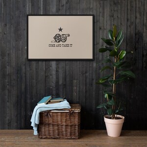 May include: A framed print of the "Come and Take It" flag, a historical symbol of the American Revolution. The flag features a cannon and a single star on a beige background.