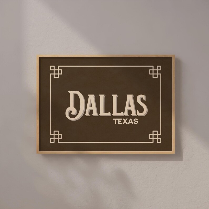 Pu&ograve; includere: Un cartello incorniciato con la parola "DALLAS" in un font vintage e "TEXAS" sotto. Il cartello ha uno sfondo marrone scuro, un bordo chiaro e una cornice in legno. Elementi decorativi angolari completano il design.