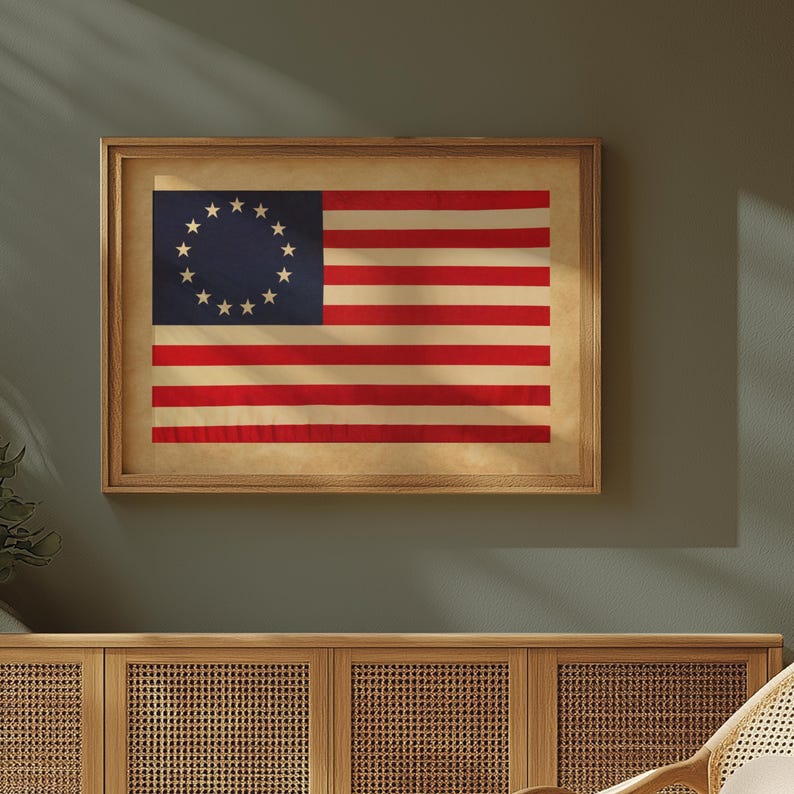 May include: Framed vintage American flag print. The flag features thirteen stars in a circle on a blue background and alternating red and white stripes. The print is in a wooden frame and hangs on a green wall.