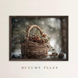 Può includere: Immagine incorniciata con un cesto intrecciato pieno di pigne e rami sempreverdi. Il cesto ha un manico e si trova in un ambiente innevato. Il testo "AUTUMN TALES" è in basso.