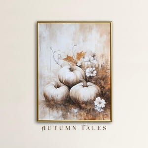 May include: A painting of white pumpkins with brown stems and leaves in a muted brown and beige color palette. The painting is framed in gold and has the text "AUTUMN TALES" at the bottom.