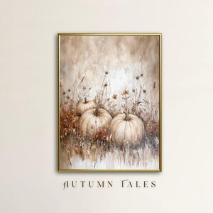 以下が含まれることがあります： 額縁に入ったアートワーク。3つの大きなクリーム色のカボチャが、乾燥した花や葉の中に描かれています。絵画は柔らかく落ち着いた色使いで、金色のフレームが付いています。「AUTUMN TALES」の文字が下部にあります。