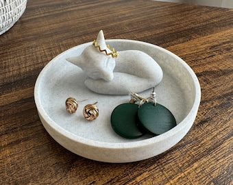 May include: A white ceramic fox ring holder with a gold ring and two pairs of earrings. One pair of earrings is gold and the other pair is green.