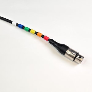 Könnte beinhalten: Ein schwarzes Kabel mit einem silbernen XLR-Stecker. Das Kabel ist mit farbigen Ringen in Weiß, Blau, Grün, Gelb, Orange, Rot und Schwarz gekennzeichnet.