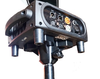 Può includere: Un faro da palcoscenico nero montato su un supporto, dotato di un pannello di controllo con porte DMX, un ingresso di alimentazione, una ventola di raffreddamento e un interruttore. La base dell'unità riporta la scritta RSR PRODUCTIONS.