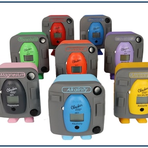 May include: Eight colorful water test kits with digital displays. The kits test for Phosphate, Alkalinity, Ammonia, Calcium, Magnesium, Salinity, and pH. Each kit has a gray base with a black button and a small, colorful container.