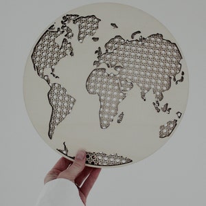 May include: A round, wooden world map with a cut-out design. The continents are removed, revealing a woven pattern within the circle. The map is held against a white background.