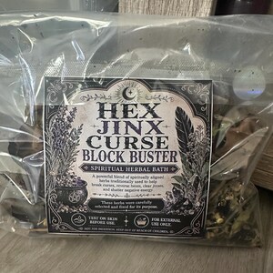 May include: A clear plastic bag containing a spiritual herbal bath blend. The label reads "HEX JINX CURSE BLOCK BUSTER" with illustrations of herbs and a cauldron. The label also includes the text "SPIRITUAL HERBAL BATH" and "FOR EXTERNAL USE ONLY."