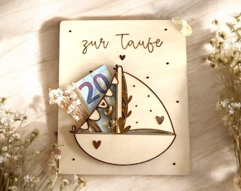 Könnte beinhalten: Holzkärtchen mit einem Segelboot-Design, die Worte "zur Taufe" sind auf die Karte graviert, und ein Zwanzigeuro-Schein ist in das Segelboot gesteckt.