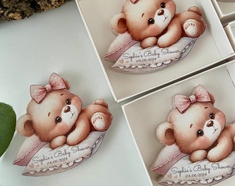May include: A wooden bear figurine with a pink bow, lying on a pillow with the text "Sophie's Baby Shower 04.06.2024".