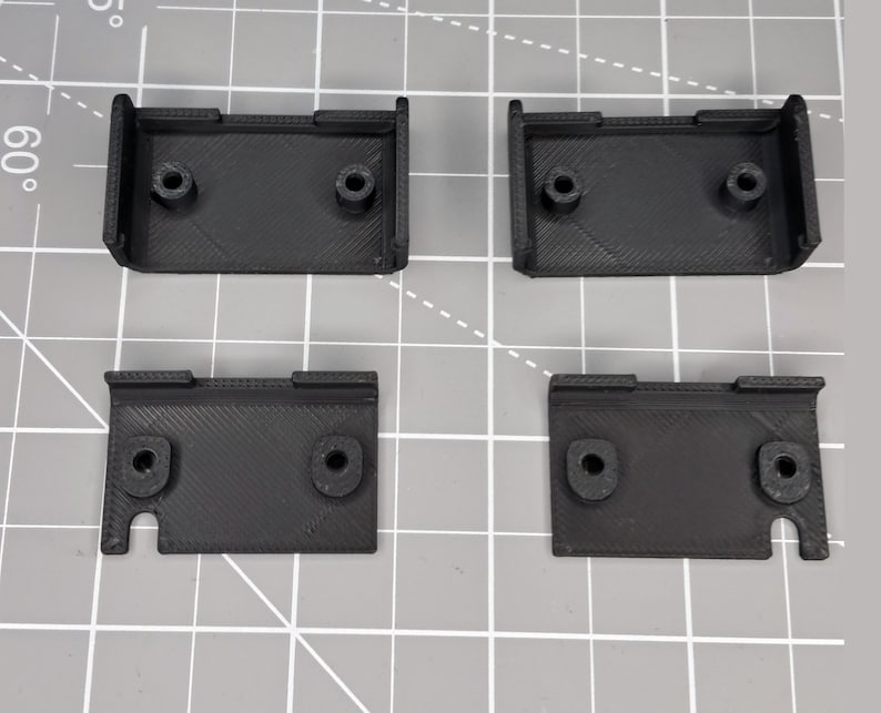 May include: Four black plastic brackets with holes for screws. The brackets are designed to be mounted to a surface.