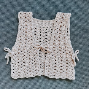May include: A crocheted cream-colored vest with a tie at the front and ties on the sides.