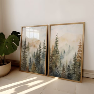 May include: Two framed watercolor paintings of a misty forest scene with tall trees in shades of green, brown, and blue. The paintings are in gold frames and are displayed on a white wall.