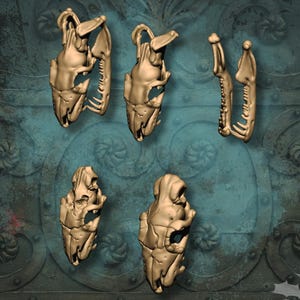 May include: A collection of gold-colored, miniature giant snake skulls. The image includes several skulls in different orientations, with the text "Essential bits" and "Giant Snake Skulls". The Etsy shop name "Olaf Miniatures" is also visible.