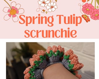 May include: A crocheted hair scrunchie in the shape of a tulip. The scrunchie is made with pink, green, and gray yarn. The scrunchie is on a person's wrist.