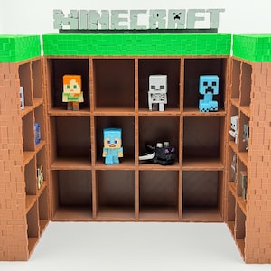 Könnte beinhalten: Ein Minecraft-Display mit mehreren Fächern. Das Gehäuse ist braun mit grünen und braunen Akzenten, und das Wort "MINECRAFT" ist oben zu sehen. Verschiedene Minecraft-Charakterfiguren werden im Inneren des Gehäuses ausgestellt.