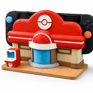 Puede incluir: Base de Nintendo Switch con forma de edificio rojo y blanco con una puerta azul y una pequeña máquina recreativa roja. La base está diseñada para parecerse a un Centro Pokémon, con una consola Nintendo Switch negra.